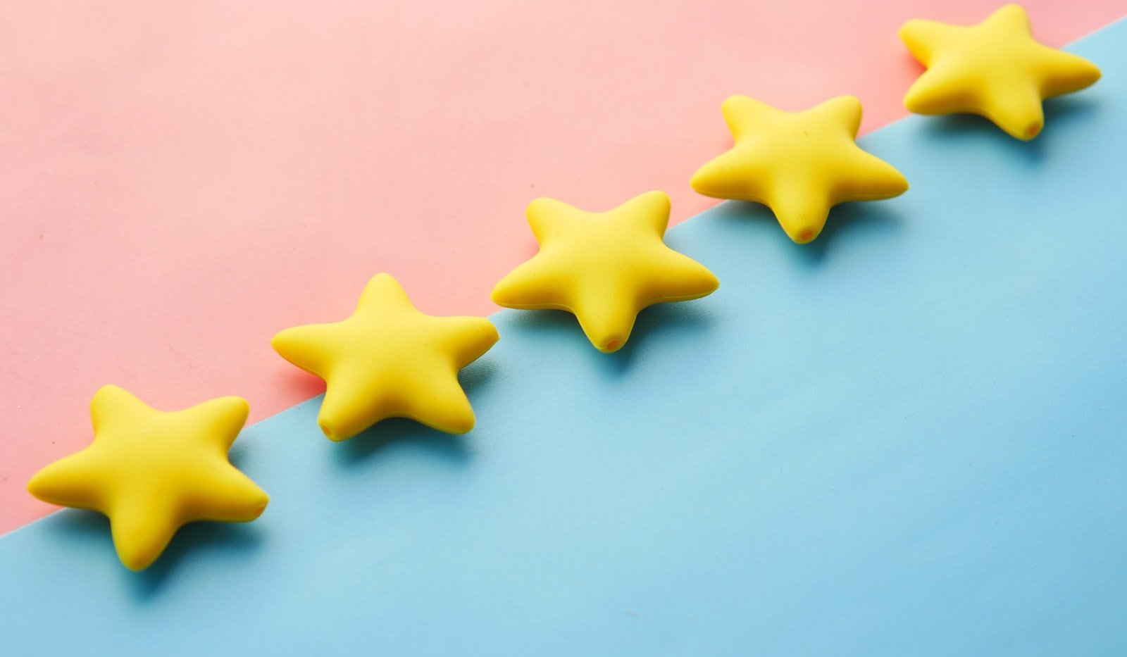 Five yellow star shaped objects arranged diagonally across a pink and blue background, evoking a five star rating display