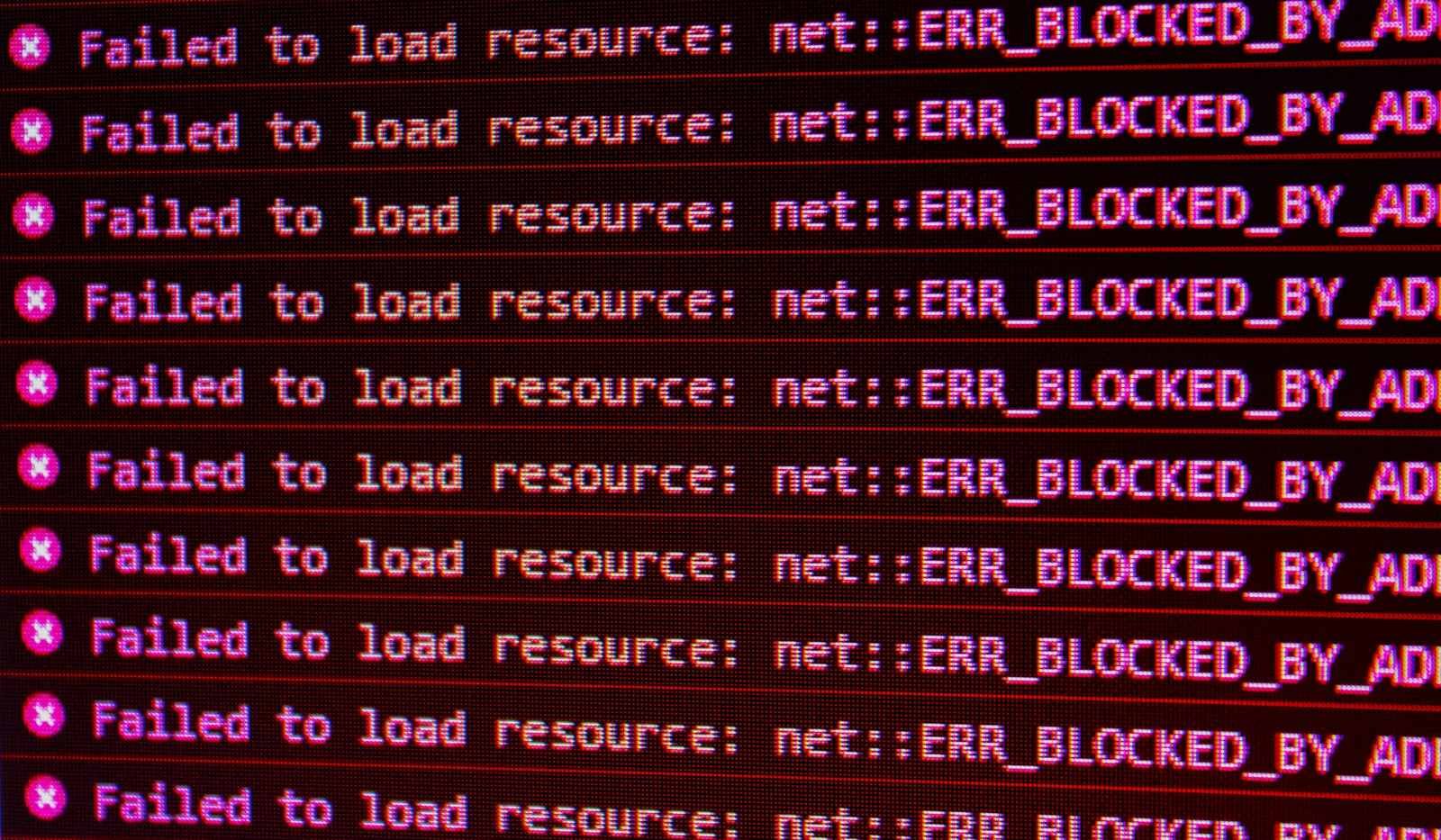 A computer screen filling with repeated red browser console errors reading failed to load resource, net colon colon error blocked by ad