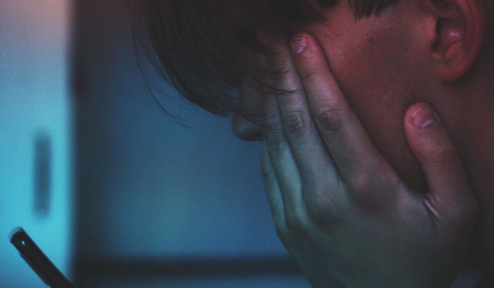 A student covering their face in distress while reading a message on their phone at night